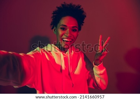 Photo of adorable funny lady dressed hoodie recording self video showing v-sign isolated red color background