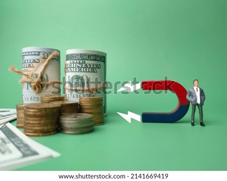 Miniature businessman attracts money using magnet on green background. Business concept.