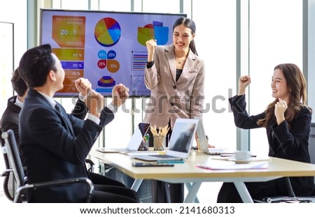 Happy excited cheerful Asian professional successful businessman businesswoman team colleagues in formal suit sitting standing in meeting room holding fists up celebrating job achievement together.