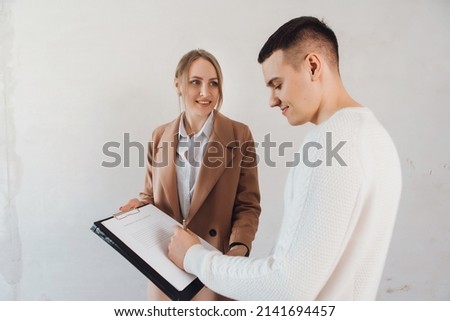 Man buying a new apartment. Satisfied man signing the contract with the saleswoman. Man buy new flat in unfinished building