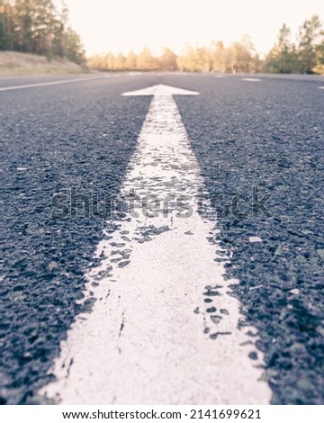 Conceptual image of an asphalt road and a direction arrow, the arrow on the road indicates the direction forward. dawn on the horizon.dawn on the way, Royalty-Free Stock Photo #2141699621
