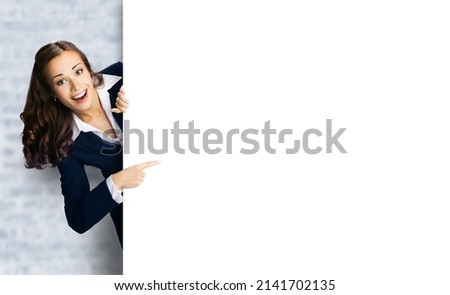 Happy excited woman in black confident suit show point finger blank white banner advertisement ad signboard billboard. Business and advertising concept. Copy space empty place. bricks loft wall.