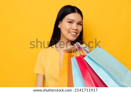 woman with Asian appearance in a yellow T-shirt with multicolored shopping bags yellow background unaltered