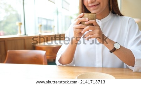 Closeup image of a beautiful young asian woman holding and drinking coffee in cafe
