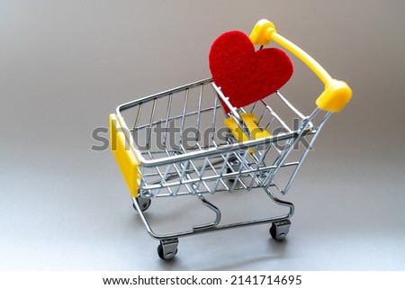 Shopping basket on a gray background with a bright red heart. Close-up.