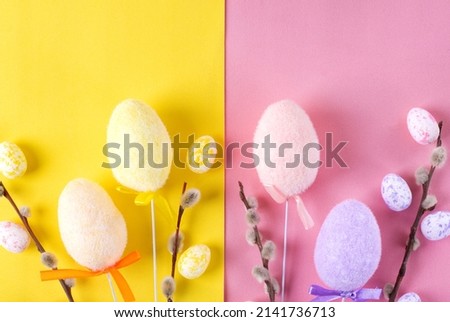 Easter flat lay with multicolored decorative eggs and willow twigs on geometric yellow and pink background