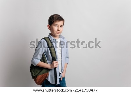 a cute serious cheerful 10 year old teenager school kid boy in glasses, blue shirt and jeans with a backpack showing a finger up isolated on white background. Education concept. Royalty-Free Stock Photo #2141750477