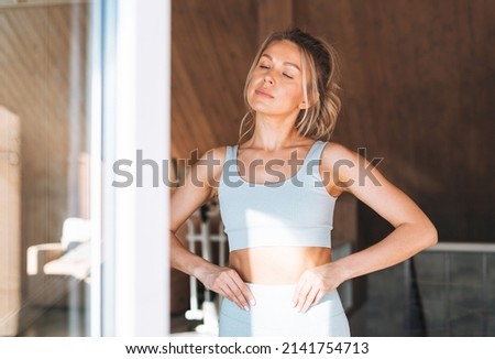 Young adult slim fitness blonde woman does morning exercises near the window of home Royalty-Free Stock Photo #2141754713