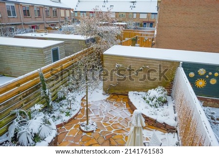 Garden with plants and colorful flagstones surprised by snow in springtime, Almere, Flevoland, The Netherlands, April 1, 2022