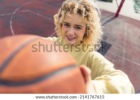 Pretty young blond European woman showing a basketball ball to the camera and smiling, standing on the sports field closeup copy space . High quality photo