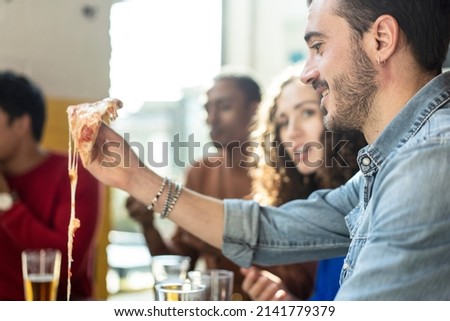 Smiling friends eating pizza at modern pizzeria restaurant - Friendship concept with multi ethnic people enjoying time together having fun at pizzeria with pizza and beer pints