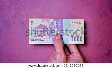 Indonesian Rupiah the official currency of Indonesia. Man's hand is making a payment. Business Saving Income Money Investment Economy and Finance Concept Uang 1000 1.000 Rupiah. One thousand Rupiah.