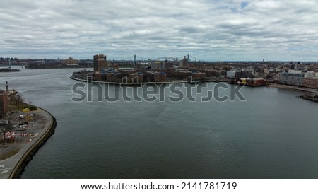 A high angle, drone view of the East River on a cloudy day. The river is still and Manhattan's Eastside and part of Queens, NY is in view.