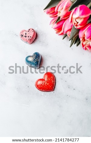 Handmade chocolates in the shape of a heart on the background of tulips. Chocolate from natrual ingredients on a light background. Creative concept for your design with a month for text