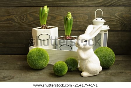 Easter decorative composition, home decoration.  On a wooden background, spring flowers, a cute rabbit, a lantern, decorative balls of greenery.  The concept of a bright Easter holiday.