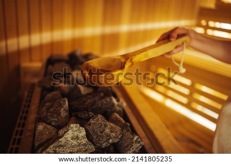 Woman in Finnish sauna, holding wooden sauna bucket. Woman is pouring water into hot stone in Sauna spa room. Woman in sauna - real, authentic moment. Royalty-Free Stock Photo #2141805235