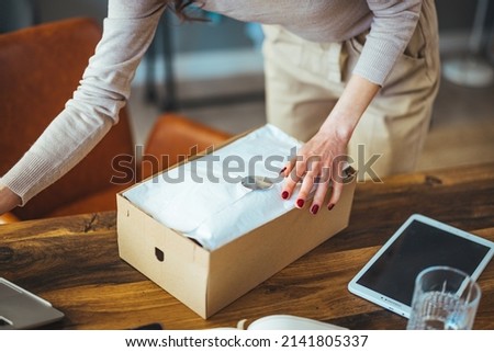 A young attractive Caucasian woman, the owner of a startup business, is looking at a new order, satisfied with the box at home, preparing to deliver a package in a wardrobe chain.