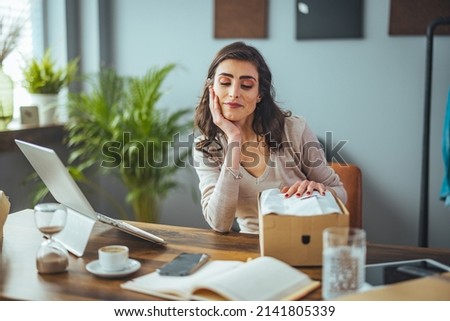 The surprised facial expressions of the girl sitting at the table in the living room open a large cardboard box and unpack the ordered goods via the internet website, she feels happy and amazed 