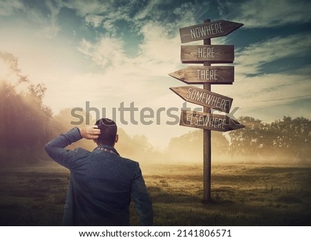 Lost and confused businessman in front of a signpost showing impossible directions. Business dilemma and difficult choice concept. Choosing the correct way on the road sign Royalty-Free Stock Photo #2141806571