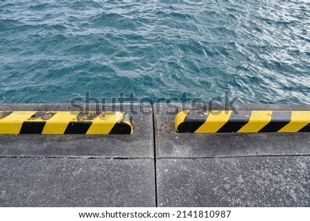 Abstract photo background of a pier with green blue water and yellow striped barriers 
