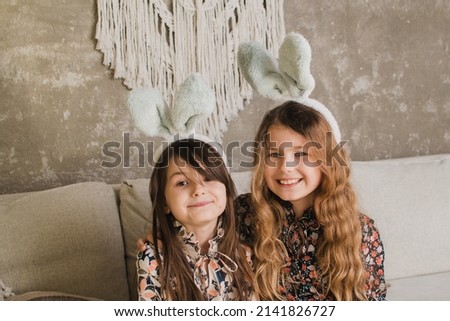 two cute little girls in rabbit ears are sitting on the sofa with Easter baskets
