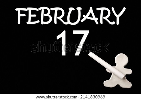 17th day of February. A small white plasticine man writing the date 17 February on a black board. Business concept. Education concept. Winter month, day of the year concept.