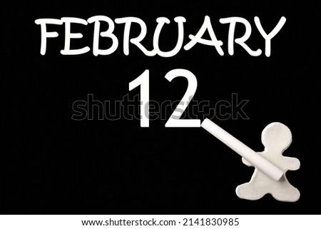 12th day of February. A small white plasticine man writing the date 12 February on a black board. Business concept. Education concept. Winter month, day of the year concept.