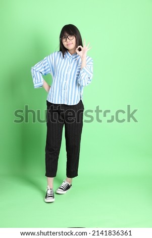 The young Asian girl in casual dressed standing on the green background.