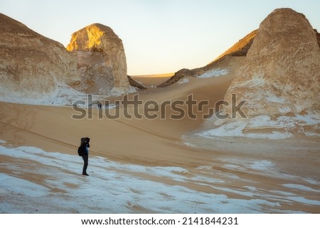 A tourist photographs sandstone formations in the white desert at dawn. Egypt
