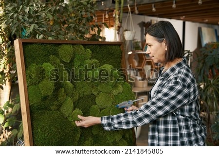 Creative woman gluing green plant on picture