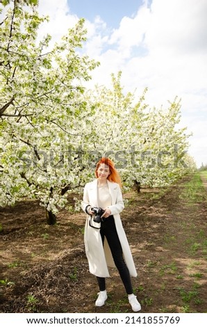 Girl photographer with red hair with a camera. female tourist, blogger, photographs nature. spring background. concept of work, hobby, tourism. spring light green tones. Royalty-Free Stock Photo #2141855769