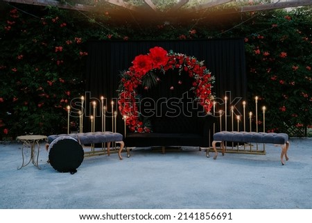 Wedding ceremony. Arch decorated with red flowers standing in the forest, henna on the wedding ceremony ground