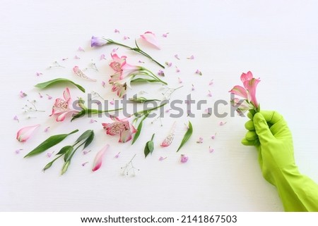 Spring cleaning concept with glove holding a flower over wooden white background