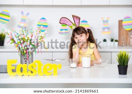 Cute little girl with bunny ears in the kitchen is smiling near the Easter cake . High quality photo