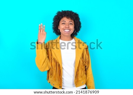 Young woman with afro hairstyle wearing yellow fringe jacket over blue background smiling and looking friendly, showing number three or third with hand forward, counting down