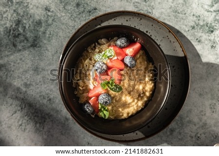 Oatmeal porridge with berries, mint and almond flakes. Trendy photography with bright sunlight and hard shadows. Sunny morning. Healthy breakfast.
