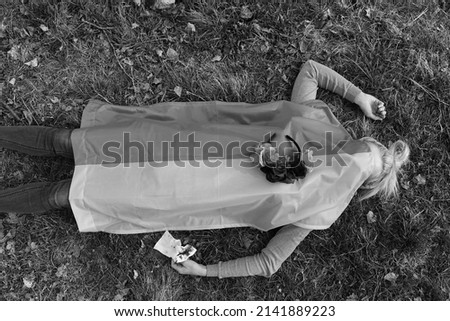 young woman lying under the ukrainian flag on the ground in nature. symbol of empathy with victimes of war conflict 2022. europe. ukraine and russia. dead girl. flower wreath.