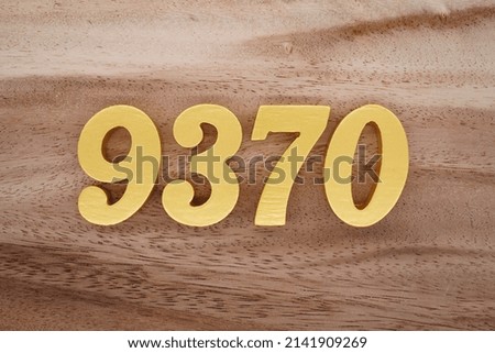 Wooden  numerals 9370 painted in gold on a dark brown and white patterned plank background.