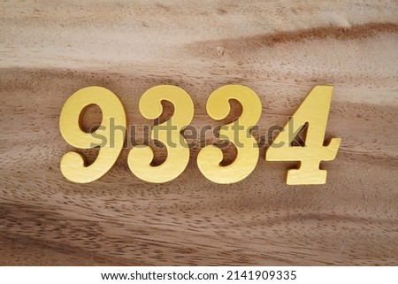 Wooden  numerals 9334 painted in gold on a dark brown and white patterned plank background.