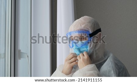 The doctor puts on a protective suit and a mask with goggles before working with those infected with the coronavirus. Danger of infection from patients with severe infection. Medic at work. Royalty-Free Stock Photo #2141911155