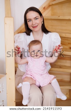 Sweet young mother playing with her little 1-year-old daughter.
Caring brunette woman sitting on wooden staircase with her small child. Tenderness and love between mother and daughter. Lovely family i