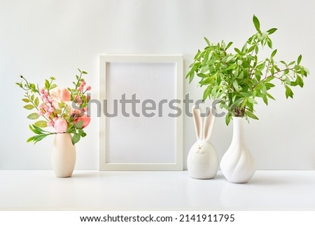 Home interior with easter decor. Mockup with a white frame and branches with green leaves in a vase on a light background