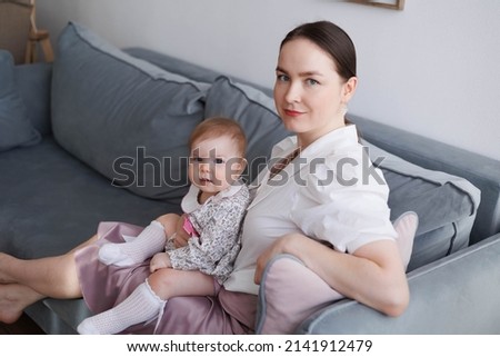 Sweet young mother holding her little 1-year-old daughter in hands.
Caring brunette woman laying with her baby child at home. Tenderness and love between mother and daughter. Lovely family indoors.
