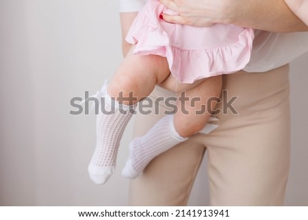 Sweet young mother holding her little 1-year-old daughter in hands.
Legs of little baby. Tenderness and love between mother and daughter. Lovely family indoors.