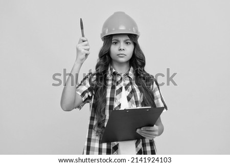serious child in construction helmet working with clipboard, under control