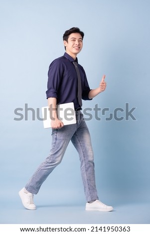 Full length image of young Asian businessman on blue background Royalty-Free Stock Photo #2141950363