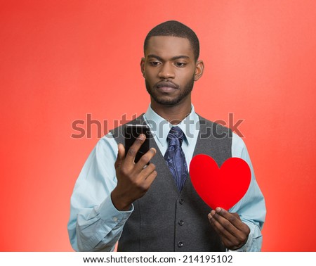 Portrait serious, thoughtful young man reading news, text message on smart phone, holding red heart isolated white background. Human facial expression, emotion feeling, body language. Social media