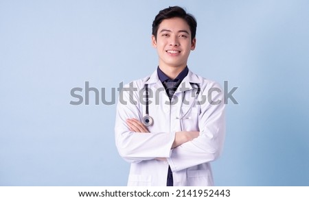 Portrait of young Asian male doctor on blue background Royalty-Free Stock Photo #2141952443