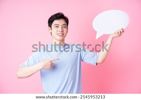 Image of young Asian man holding message bubble on pink background