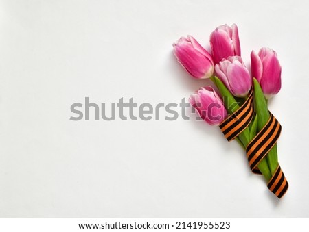 Pink tulips with St. George ribbon isolated on white background. Victory day or Fatherland defender day. Greeting card for holiday. Copy space, flat lay 